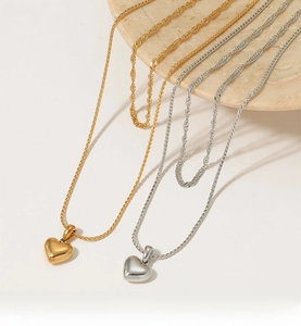 Détail de colliers superposés avec pendentifs cœur en or et argent sur marbre blanc