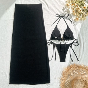 Flat lay of black three-piece bikini set with sheer mesh maxi skirt and beach accessories