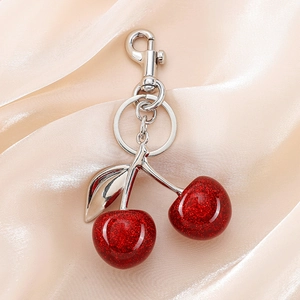 Close-up of glittery red cherry keychain with silver leaves on soft peach silk fabric