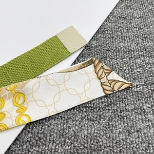 Close-up of green woven canvas belt and silk scarf with golden chain pattern