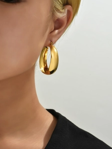 Close-up of chunky gold hoop earrings in polished stainless steel on a model's ear