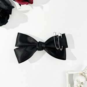 Detail of black satin bow hair clip with silver safety pins in gothic aesthetic