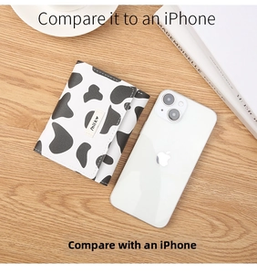 Mini cow print wallet next to iPhone on wooden table showing compact portable size