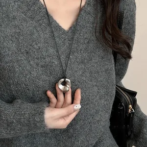 Irregular silver pendant on black cord shown over a textured grey knit sweater
