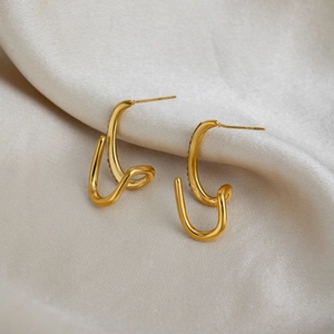 Irregular wavy line earrings in 18K gold plated stainless steel on white fabric background