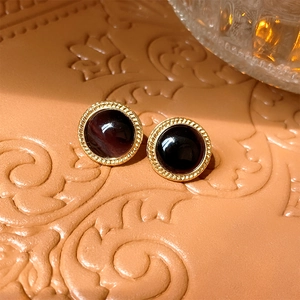 Close-up of vintage round cat-eye earrings with gold textured edges on orange background
