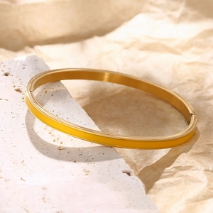 Detail of a gold stainless steel bangle with yellow enamel on a textured stone background