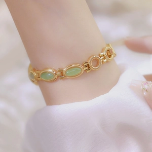 Close-up of gold chain watch with green jade stones worn on a female wrist