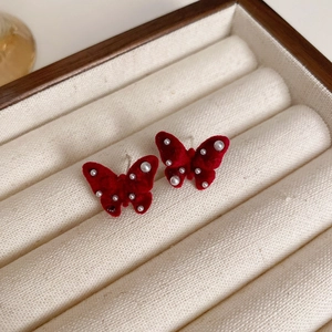 Close-up of red velvet butterfly stud earrings with white pearls in a jewelry box