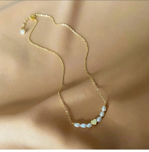 Detailed view of freshwater pearls and golden heart pendant on champagne silk fabric