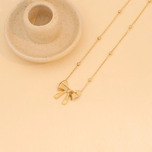 Detail of a polished gold bow pendant on a delicate beaded chain over a beige background