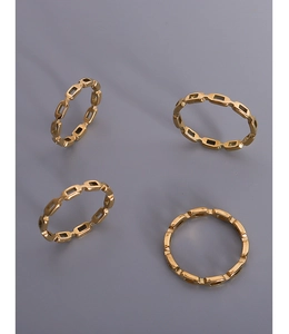 Detail of four golden minimalist hollow chain rings on a sleek grey background with shadows