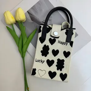 Detail of knitted phone bag with heart and bear patterns, black handle, and metal snap closure