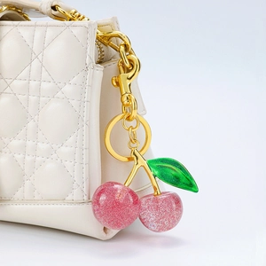 Detail of pink glitter cherry keychain pendant on a white quilted leather handbag