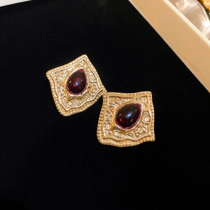 Detailed close-up of vintage gold earrings with embossed patterns and red gemstones