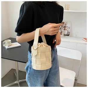 Detail of cream woven bucket bag featuring gold ring handle and minimalist texture