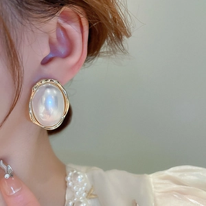 Gros plan d'une boucle d'oreille en perle ovale dorée portée par un mannequin de style rétro