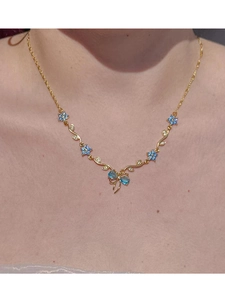 Nahaufnahme der goldenen Kette mit blauen Kristallblüten und einem Schmetterlingselement