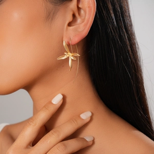 Macro close-up of golden iris flower drop earrings worn on a model's ear