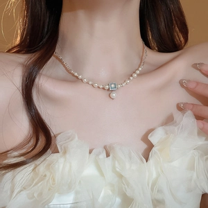 Detailed close-up of pearl necklace with blue gemstone pendant on a model neck