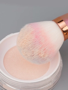 Macro view of fluffy powder brush head with pink gradient bristles dipping into fine powder