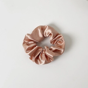 Close-up of champagne silk satin scrunchie with elegant pleated texture and soft luster