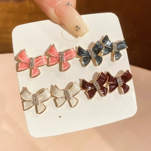 Detail of four pairs of bow-shaped stud earrings in pink, blue, white, and burgundy colors