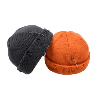 Pair of distressed knit beanies with metal safety pins in dark gray and orange colors.