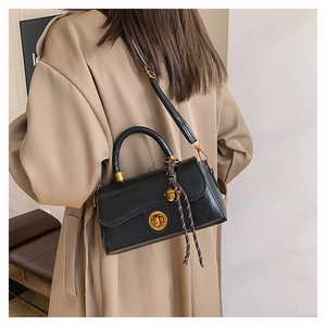Detail of black leather crossbody bag with gold buckle and decorative woven charm