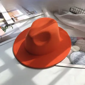 Detail view of a stylish orange wide-brim wool fedora hat on a minimalist white surface