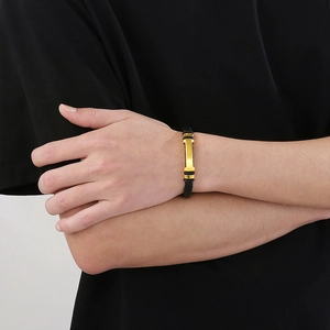 Close-up of black braided leather bracelet with a polished gold curved metal plate