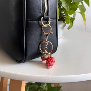 Close-up of vibrant red strawberry keychain charms on black bag with golden metal ring