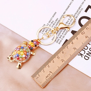 Close-up of golden turtle keychain with colorful beads and rhinestones on satin background