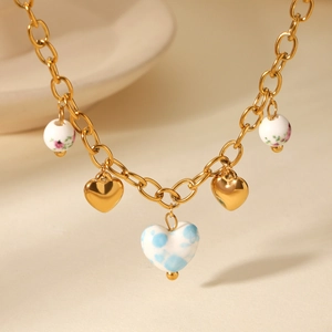 Close-up of gold chain necklace with ceramic floral beads and heart charms