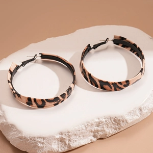 Detail shot of leopard print leather wrapped hoop earrings on a marble stone base
