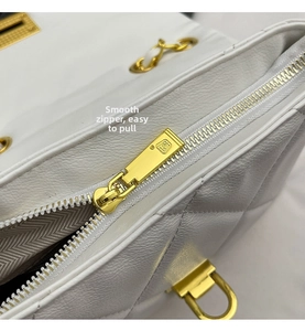 Close-up of white quilted leather bag featuring a smooth gold metal zipper and chain detail