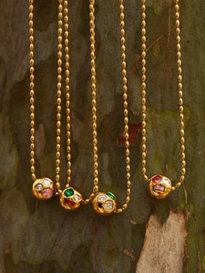 Détail de quatre colliers dorés avec zircons colorés suspendus devant une écorce naturelle
