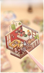 Close-up of a mini cat-themed scrapbook sticker book being held with pink tweezers