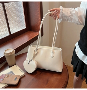 White minimalist tote bag with heart charm and strap on a wooden table setup