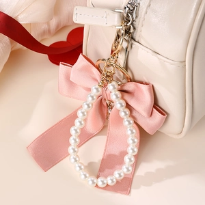 Close-up of pink ribbon bow and pearl pendant with gold metal clasp on white leather bag