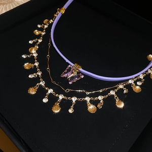 Layered butterfly choker with purple cord and golden shell pendant on black jewelry box