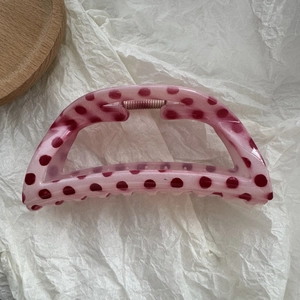 Close-up of a large translucent pink resin hair claw with red polka dots on white paper