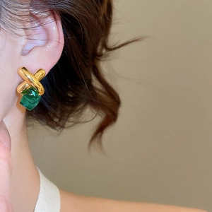 Detail of cross pattern earrings with emerald cut green stone on model's ear