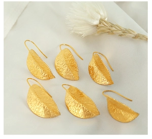 Detailed macro view of gold leaf earrings with intricate mesh texture on white fabric