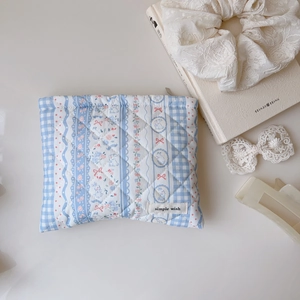 Pochette matelassée à carreaux bleus, motifs floraux et lapins sur bureau blanc