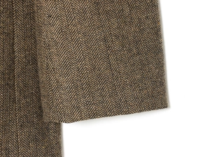 Close-up of brown herringbone tweed fabric texture on a fashion blazer sleeve