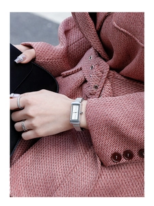 Detail of silver square watch with mesh strap worn on wrist against a pink coat