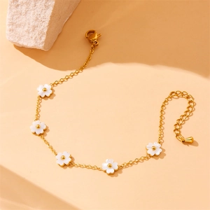 Golden chain bracelet with white flower charms on a textured stone over an orange background
