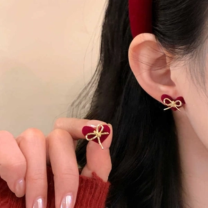 Close-up of a red flocked heart earring with a golden bow detail worn by a model