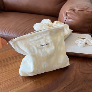 Textured off-white bubble fabric cosmetic bag with simple wish label on a wooden table